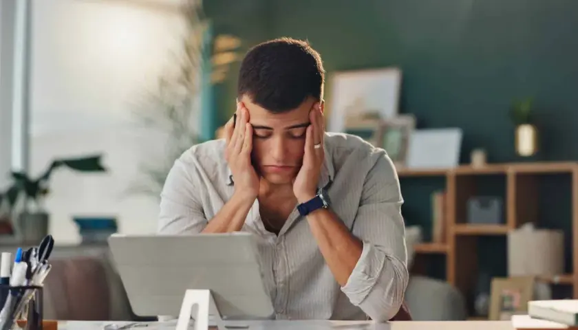Un homme stressé se tient la tête devant une tablette.