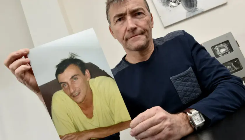 Un homme tient une photo d'un jeune homme en t-shirt jaune. Il semble chercher des réponses, se demandant sans nouvelle d'une personne que faire.