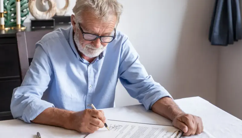 Un homme âgé signe un document, peut-être un modèle de lettre pour annuler un testament.
