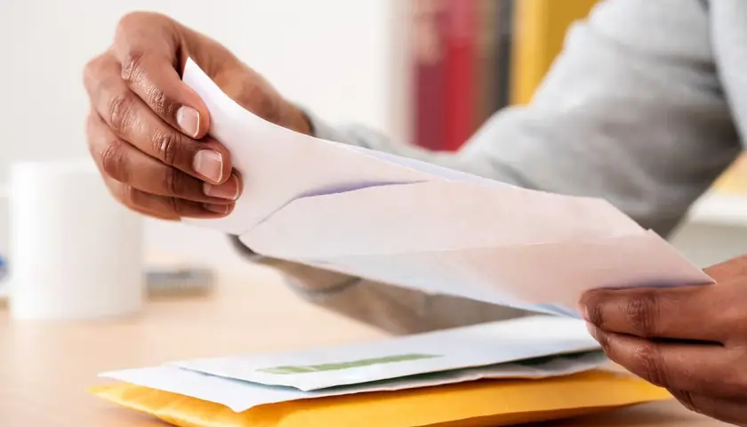 Mains ouvrant des enveloppes, peut-être une arnaque au chèque énergie ? Attention aux courriers suspects.