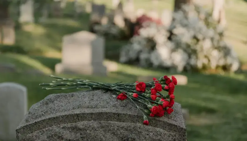 Un bouquet de fleurs rouges repose sur une pierre tombale dans un cimetière. Une question se pose : peut-on acheter une concession de son vivant ?