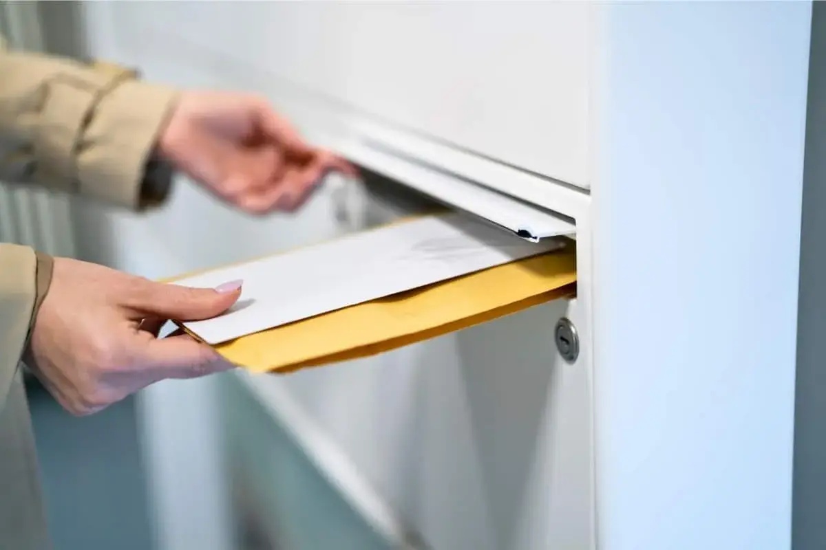 Main tenant insère des enveloppes dans une boîte aux lettres. Le délai recommandé pour la réception est important.