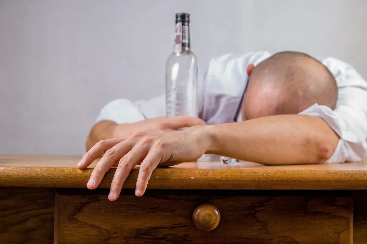 Un homme endormi sur son bureau, une bouteille vide à côté. Les conséquences de l'alcool au travail sont visibles.