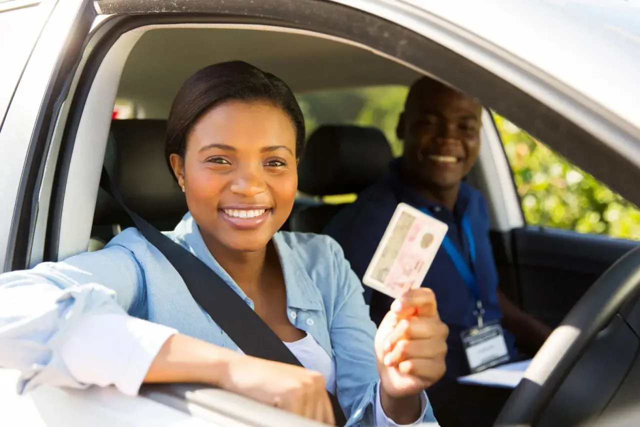 Une jeune femme souriante tient son permis de conduire, fière de sa réussite. L'auto-école veille à la répression des fraudes pour des formations honnêtes.