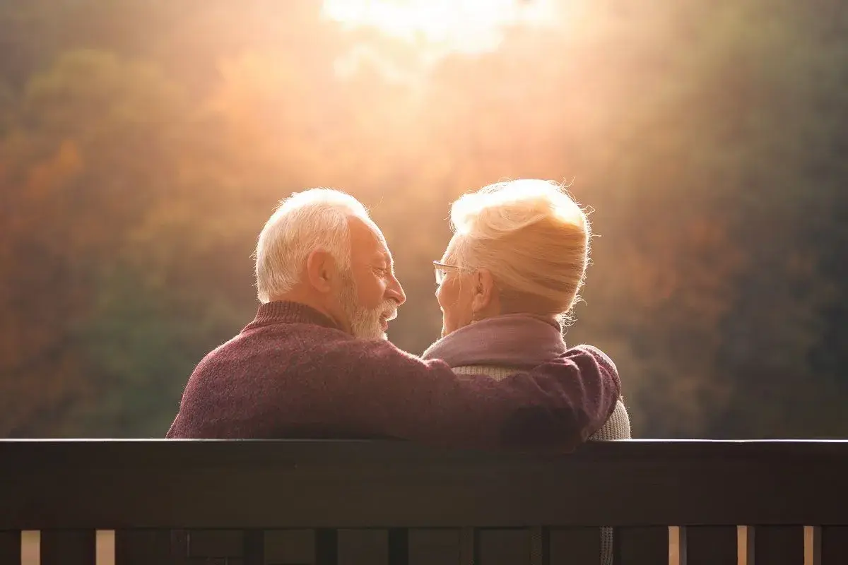 Couple âgé regardant le soleil couchant, bras autour des épaules.