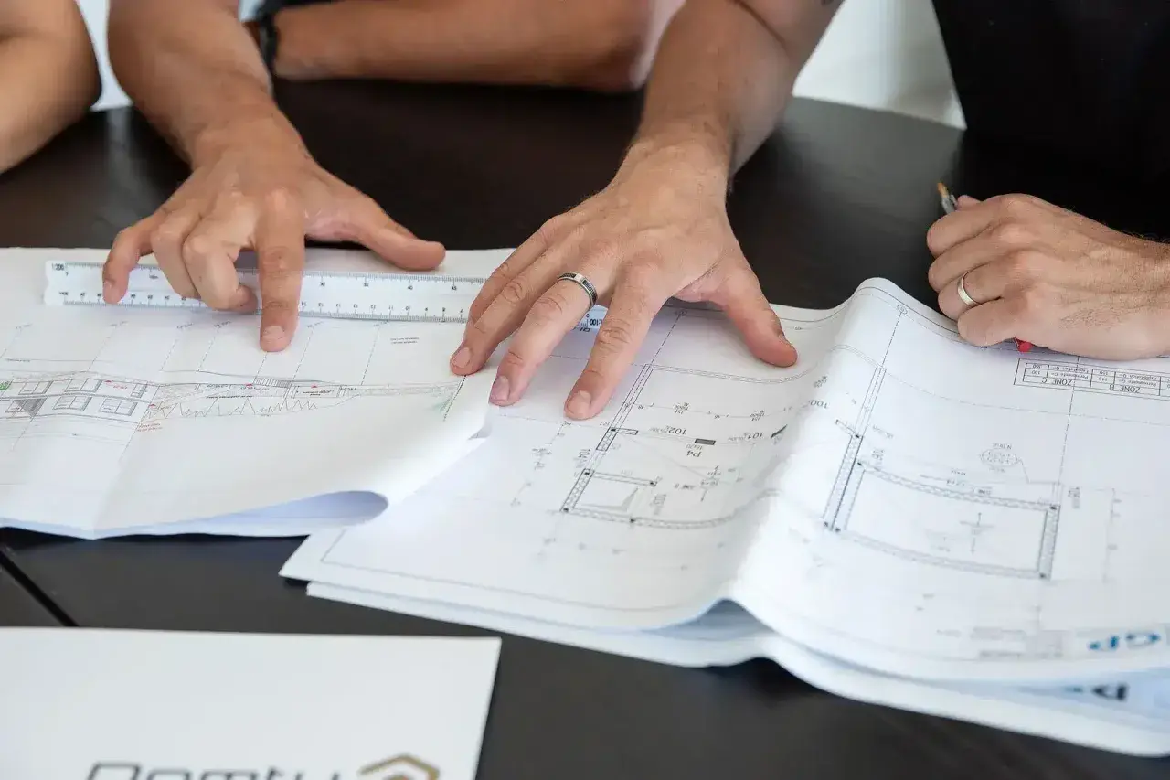 Des mains travaillent sur des plans d'architecte, une règle à la main. Comprendre ces détails est essentiel pour savoir pourquoi faire un devis précis.