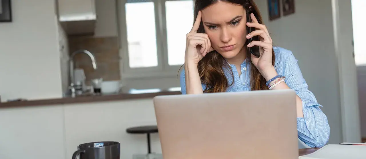 Femme soucieuse au téléphone, devant son ordinateur, envisageant de porter plainte contre une entreprise.