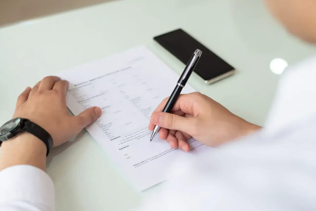 Un homme remplit un formulaire, peut-être un cerfa, pour une demande. Il utilise un stylo pour signer.