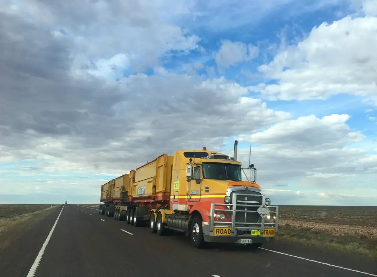 Un long camion jaune, un "road train", roule sur une route déserte sous un ciel nuageux. Ce véhicule est essentiel pour la convention collective transport.