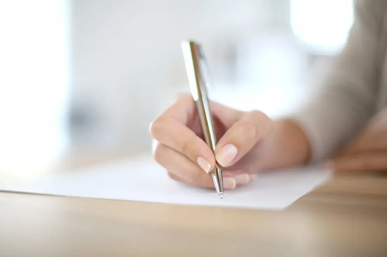 Main d'une personne écrivant avec un stylo sur un document.