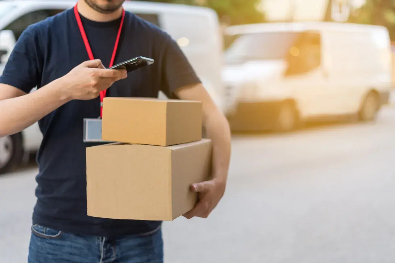 Livreur avec colis, vérifiant son téléphone. Un retard de livraison peut être une violation du code de la consommation.