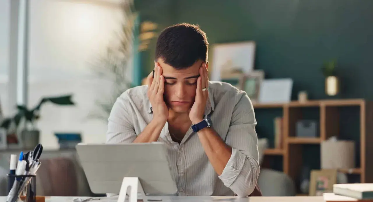 Un homme stressé se tient la tête devant une tablette.