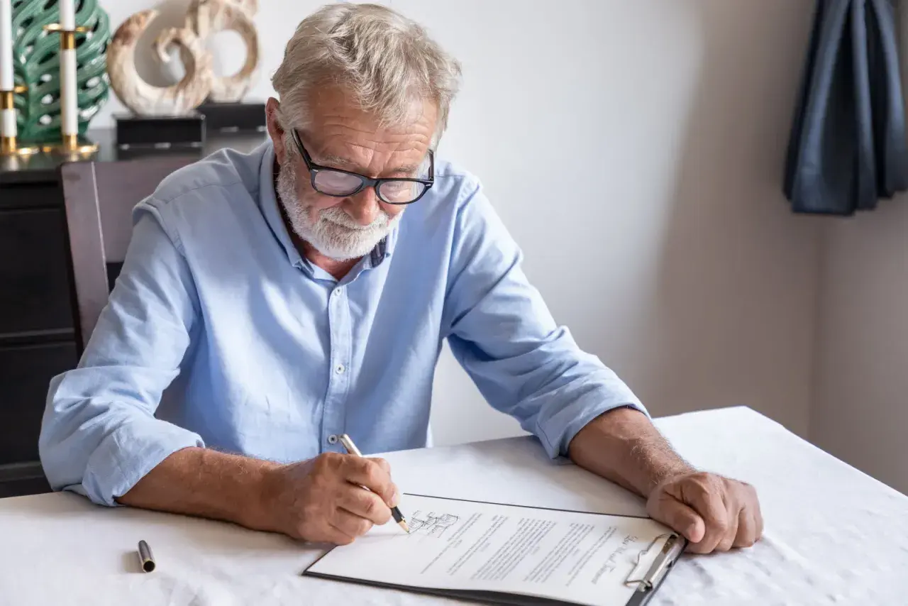 Un homme âgé signe un document, peut-être un modèle de lettre pour annuler un testament.