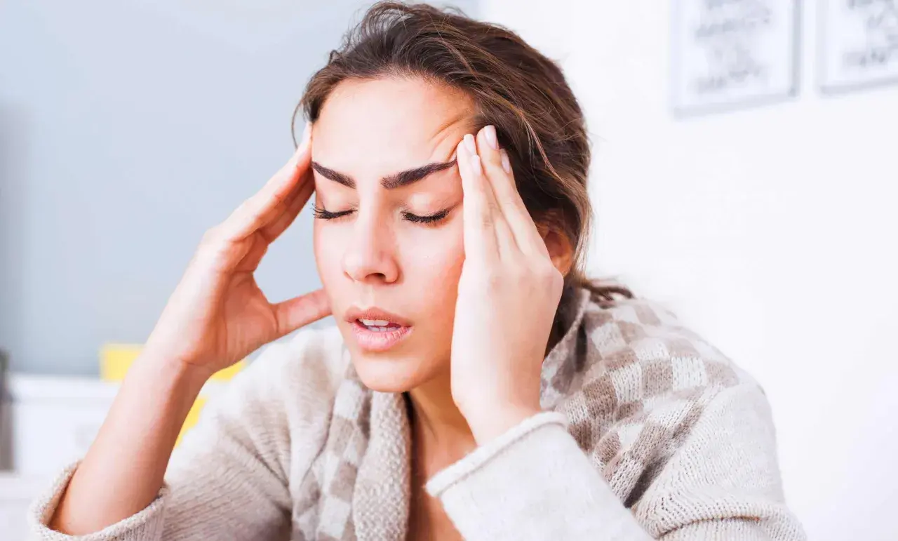 Femme se tenant les tempes, l'air soucieux. Comment toucher 100 % de son salaire en arrêt maladie ?
