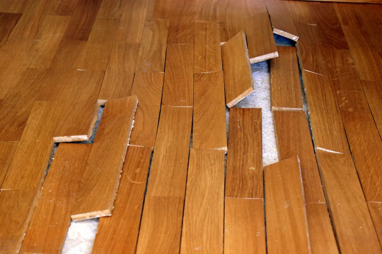 Parquet en bois abîmé, lames décollées et cassées. Une vraie malfaçon de travaux qui rend le sol dangereux.