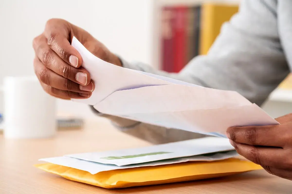 Mains ouvrant des enveloppes, peut-être une arnaque au chèque énergie ? Attention aux courriers suspects.
