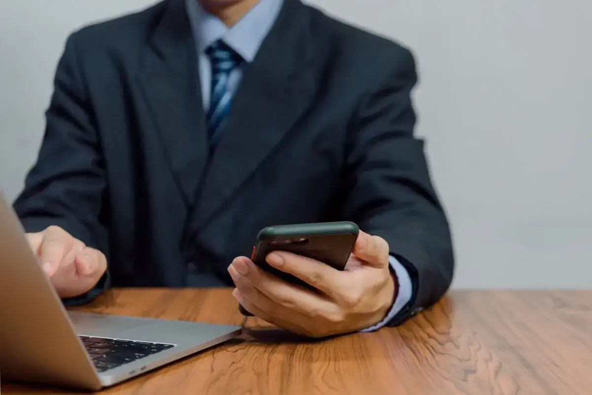 Un homme en costume utilise son téléphone, peut-être victime d'usurpation d'identité par téléphone.