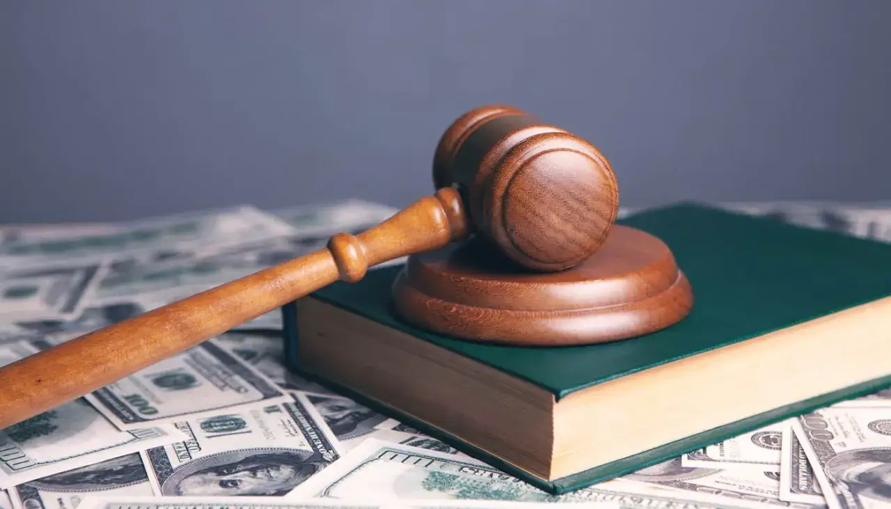 Marteau de juge sur un livre vert, entour&eacute; de billets de dollars. Une image symbolisant la n&eacute;cessit&eacute; de demander au notaire une avance sur succession.
