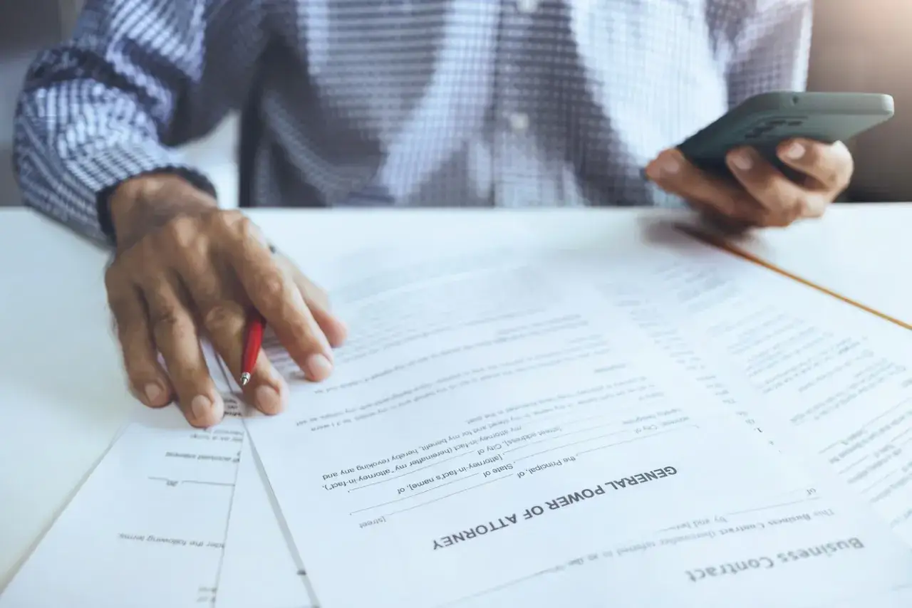 Main tenant examine un document de procuration et contrat, son t&eacute;l&eacute;phone &agrave; la main. Il pourrait s'agir d'une affaire de procuration et d&eacute;tournement.