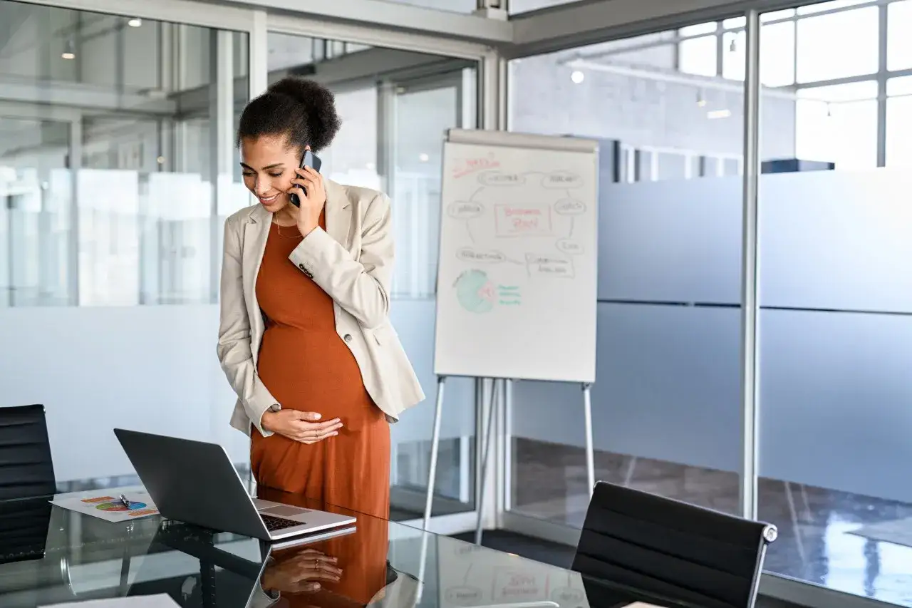 Femme enceinte au t&eacute;l&eacute;phone, discutant de la r&eacute;duction du temps de travail pour la grossesse, devant un tableau blanc.