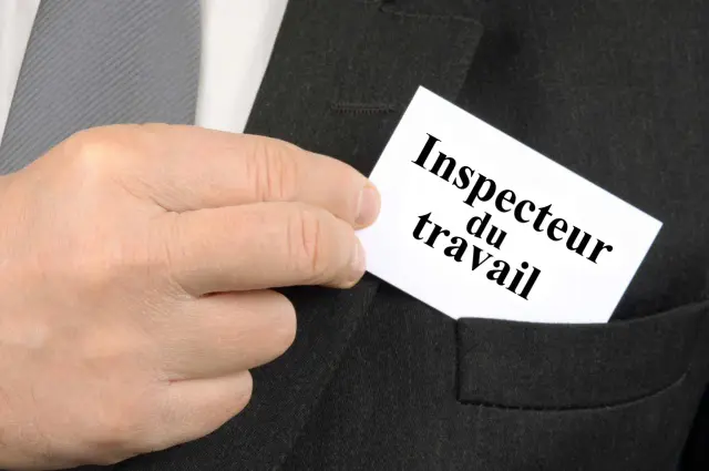 Une main glisse une carte "Inspecteur du travail" dans la poche d'un costume.